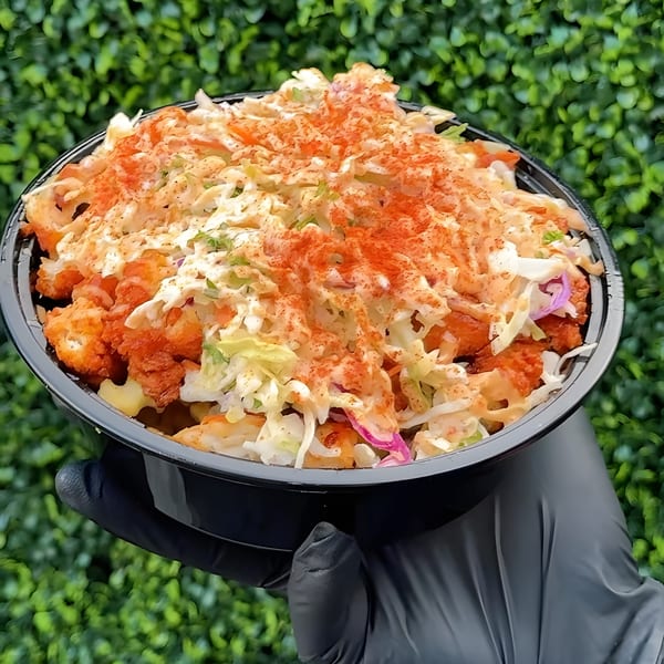 A black gloved hand holds a bowl of Five Star Chicken's fried chicken, coleslaw, and paprika.